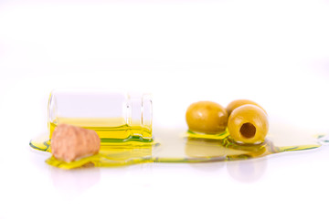 Macro shot of a small bottle of premium virgin olive oil spilled and olives on white background. Focus is on the olives