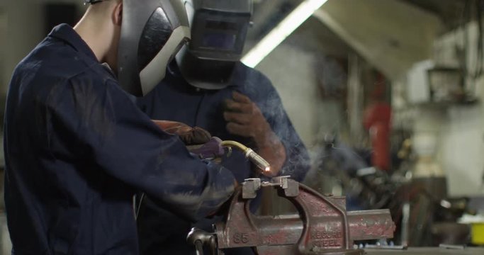 4K Portrait young apprentice welder & senior colleague smiling at camera. Slow motion.