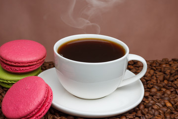 white cup of coffee with steam on a brown background on coffee beans with pink and green cookies