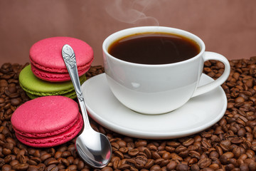 White coffee cup with hot coffee with a spoon of pink green pastry on coffee beans.