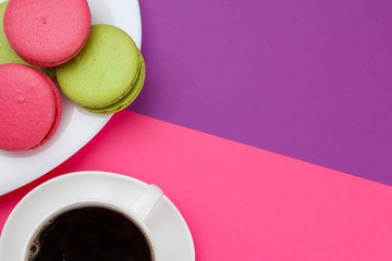A cup of coffee and dessert on a pink-violet background with green and pink cookies.