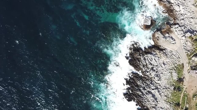 Drone approaching the rocky seashore near Sferracavallo village, Palermo province, Sicily, Italy, with waves dashing on the rocks