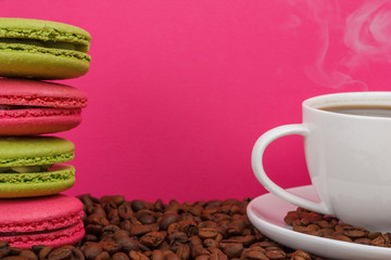 Pink and green cookies on coffee beans with a cup of coffee on a pink background.