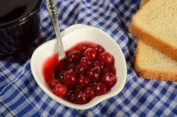 FRESH JAM FROM THE CRANBERRIES IN WHITE BOWL WITH SPOON TWO PIECES OF TOAST BREAD AND A MUG OF TEA