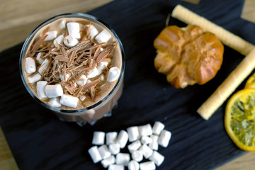 Cocoa with marshmallow in rock glass on a wood black tray with cake and lemon. Close-up top view