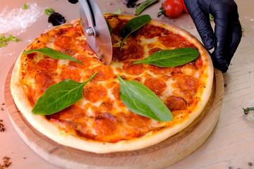 Cook takes a slice of salami pizza with spinach leaves, hands in rubber gloves close-up view