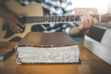 Close up the old Bible with young male playing guitar acoustic at background. Christian worship God...