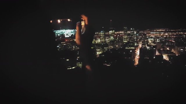 A young girl photographs the city at night with her smartphone