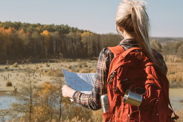 Country journey. Back view of lady with backpack using map to explore country. Fall landscape background.