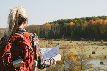 Tourism and adventures. Back view of lady with backpack using map to explore country. Fall landscape background.