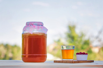 Kombucha  in a jar on a light wooden table against the sky, a glass filled with Kombucha   with raspberries.