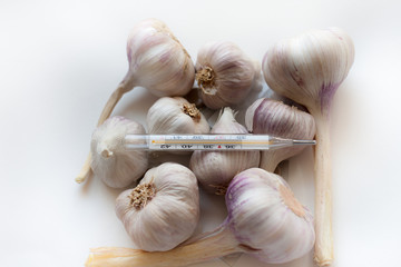 A lot of garlics with  glass mercury thermometer and pills on white table. Top view. Flat lay.