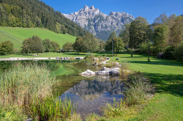 Public biotope swimming pool lake in Verfenweng surrounded by Alps, beautiful rocks in water level reflection, amazing greenery