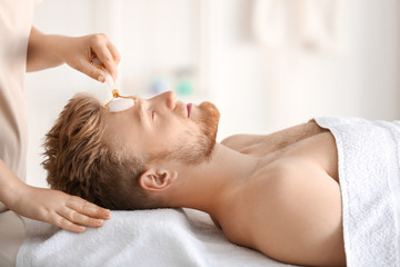 Fototapeta na wymiar Handsome young man receiving facial massage in spa salon