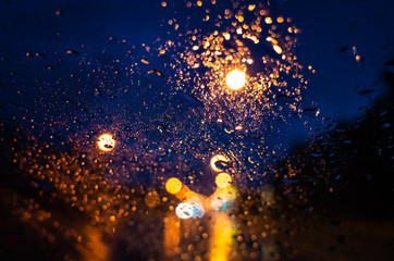 The bright lights of the night city through the glass in the drops of rain. Photo for background.