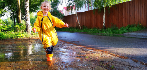 A little cute girl in a yellow waterproof jumpsuit having fun running and jumping through puddles...