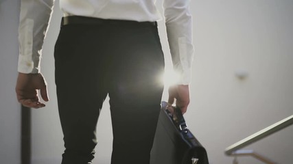 Slow motion footage: Unrecognizable businessman or lawyer in formal suit with briefcase goes down stairs from meeting. Concepts: The end, happy end, success, finish