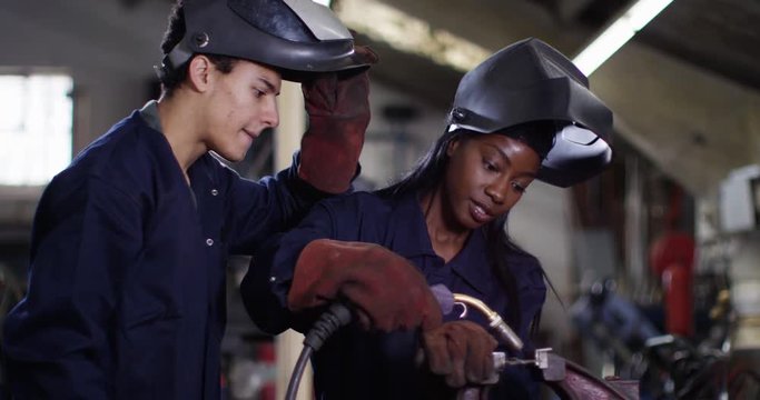 4K Female welder in factory workshop giving training to young apprentice. Slow motion.