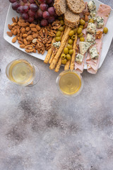 Two glasses of white wine and plate with different snacks. Blue cheese, olives, baguette slices, grissini, ham, grapes and nuts. Wine snacks set background.