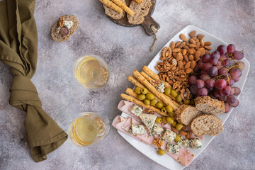 Two glasses of white wine and plate with different snacks. Blue cheese, olives, baguette slices, grissini, ham, grapes and nuts. Wine snacks set background.