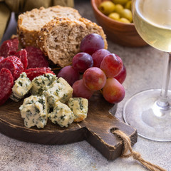  Charcuterie board with different snacks for wine. Blue cheese, olives, baguette slices, cured meat and  grapes Wine snacks set background.