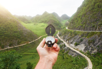 Compass in the hand of the traveler the background of roads in the mountains.