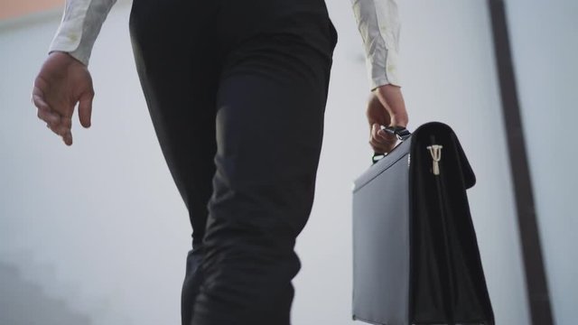 Businessman with briefcase walking across the office building. Close up. 4K