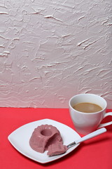 Curd jelly on the surface of coral color. Dessert lies on a plate, a piece in a spoon. Nearby is a cup of coffee. Against the background of white wall with decorative plaster.