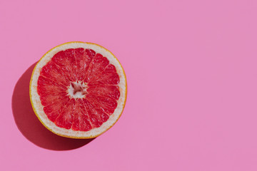 Fresh cutted grapefruit on a pastel pink background closeup at the left side of the table