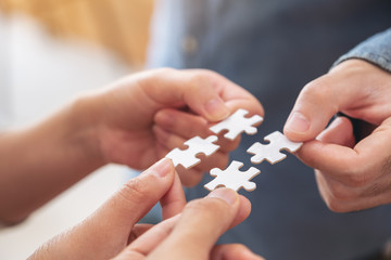 Closeup image of people's hands holding and putting a piece of white jigsaw puzzle together