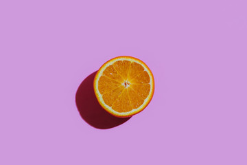 Fresh cutted orange on a pastel violet background at the center of the rectangular table