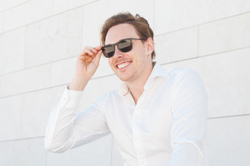 Happy business man adjusting sunglasses outdoors. Guy looking away with building wall in background. Business man portrait concept.