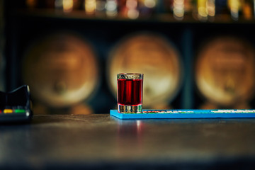 shot with a red drink on the background of a bar with oak barrels
