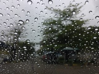 The raindrops on the windscreen or windshield or car glass. View from the inside of the car with a grey sky background