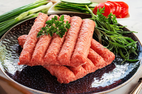 Chevapchichi is a national Balkan dish. Close up a row of fresh raw beef kebabs.