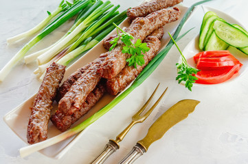 grilled Cevapcici is a Balkan national dish. Close the row of fried beef kebabs on a white rectangular dish with vegetables