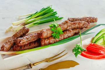 grilled Cevapcici is a Balkan national dish. Close the row of fried beef kebabs on a white rectangular dish with vegetables