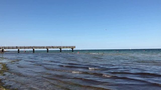 Beautiful wooden pier on the horizon. Small waves on the sea coast. Iphone video