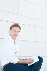 Portrait of handsome entrepreneur writing in planner. Positive Caucasian businessman sitting outdoors and writing thoughts in journal