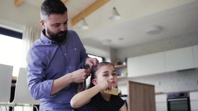 Mature father with small daughter indoors at home, plaiting hair.