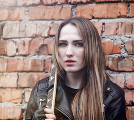 Beautiful young girl rocker with electric guitar. A rock musician girl in a leather jacket with a...