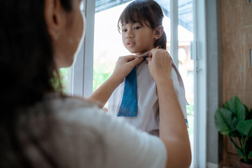mom help to put on uniform on her daughter in the morning before going to school