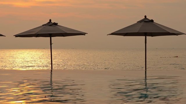 Pink orange yellow reflection in infinity pool and sea on sunset, Umbrellas.