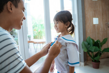 happy kid wearing school uniform her father help her to button the shirt on