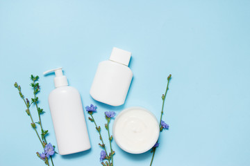 White jars of cosmetics with flowers on a blue background. Bath accessories. Face and body care concept. Top view