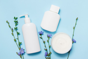 White jars of cosmetics with flowers on a blue background. Bath accessories. Face and body care concept. Top view