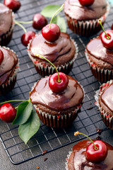 Cherry-Chocolate-coffee muffins with melted dark chocolate topping with the addition of fresh cherries on on a cooling tray, on a dark background, close-up. Delicious dessert