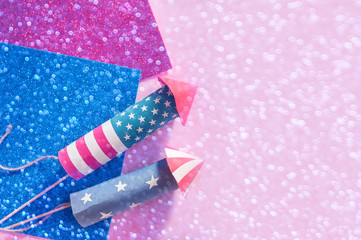 4th July holiday shopping concept. Shopping bags in national american colors and firework rockets over pink background