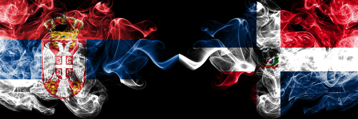 Serbia vs Dominican Republic smoky mystic flags placed side by side. Thick colored silky smokes combination of Serbian and Dominican Republic flag