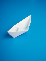 Single white paper boat on a blue background
